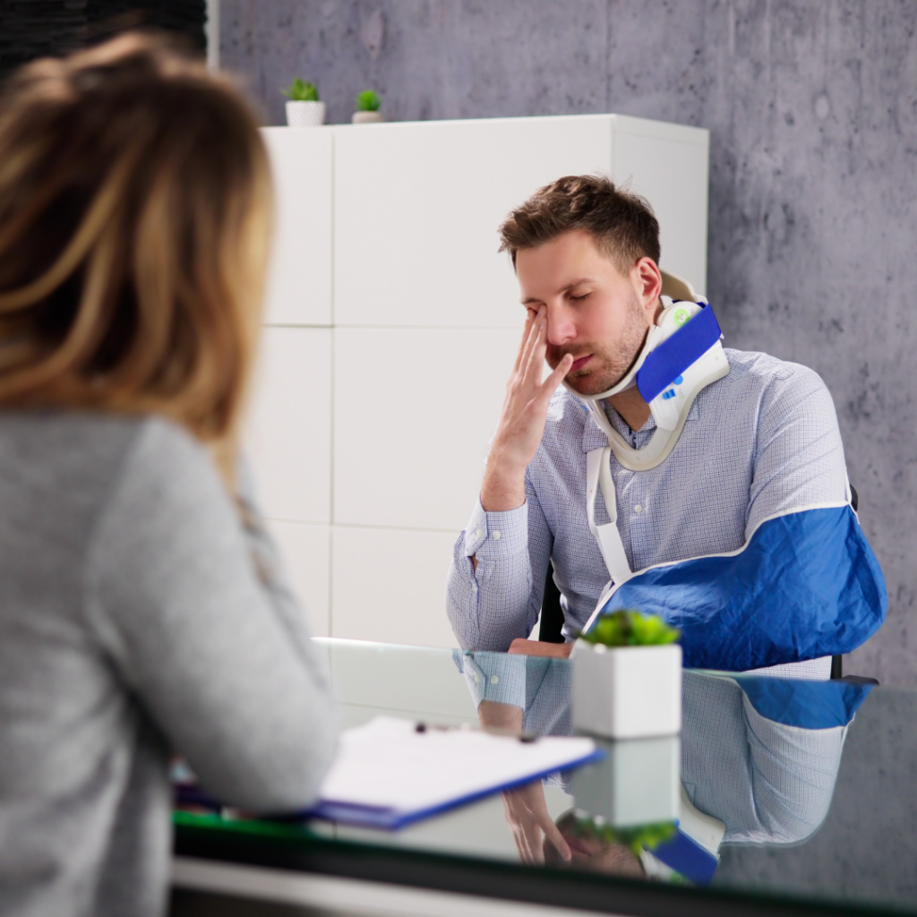 Person in a neck brace and arm sling sitting across from another person at a desk.
